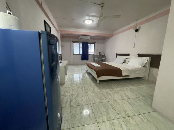 A hotel room with a bed, a desk, a chair, a ceiling fan, and a blue refrigerator. - OYO 75494 President Apartment (Pattaya)