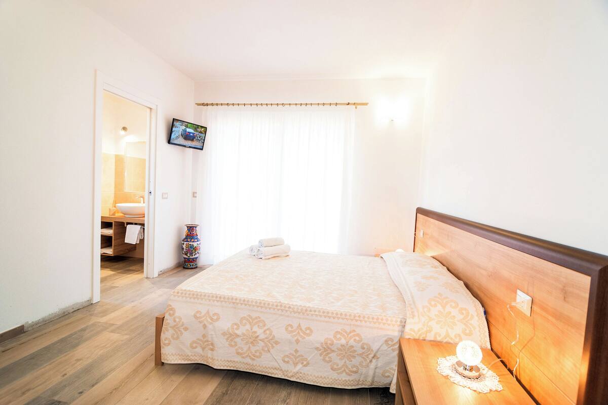 A hotel room with a bed, bedside table, TV, and a bathroom visible through an open door.