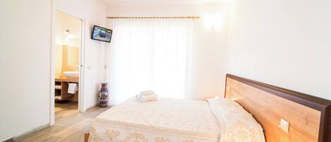 A hotel room with a bed, bedside table, TV, and a bathroom visible through an open door.