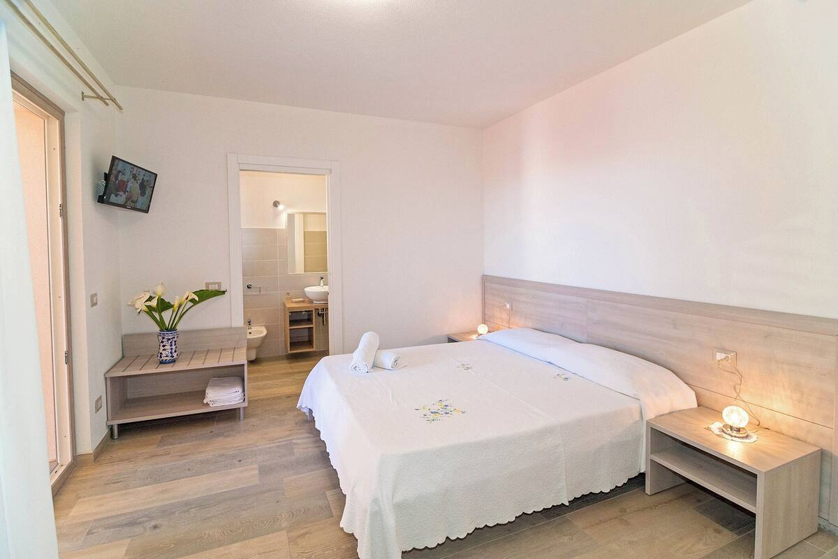 A neatly arranged bedroom with a bed, bedside tables, a small bench, and a vase with flowers.