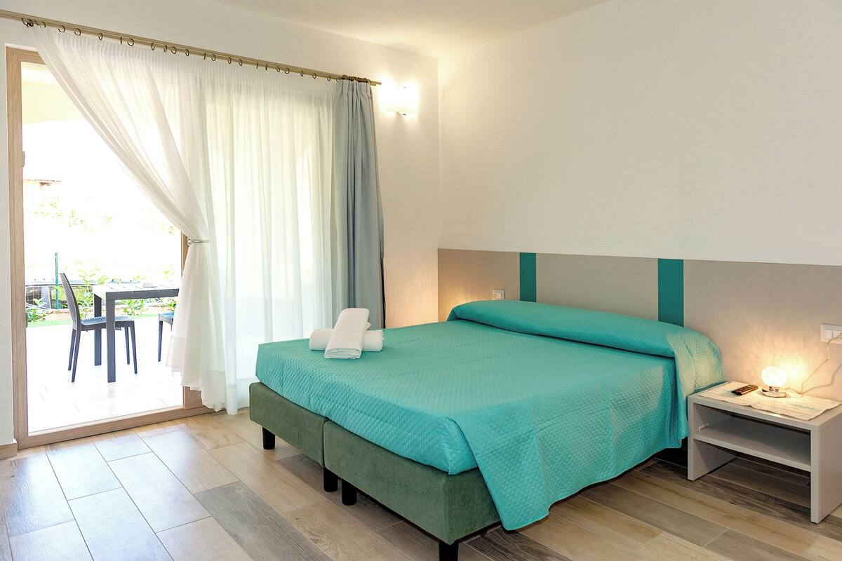 A bedroom with a bed, a nightstand, a chair, and a view of the outdoors.