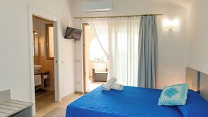 A bedroom with a blue bedspread, a single pillow, and a television mounted on the wall. - MOLAROTTO CAMERE CON ANGOLO COTTURA (San Teodoro)