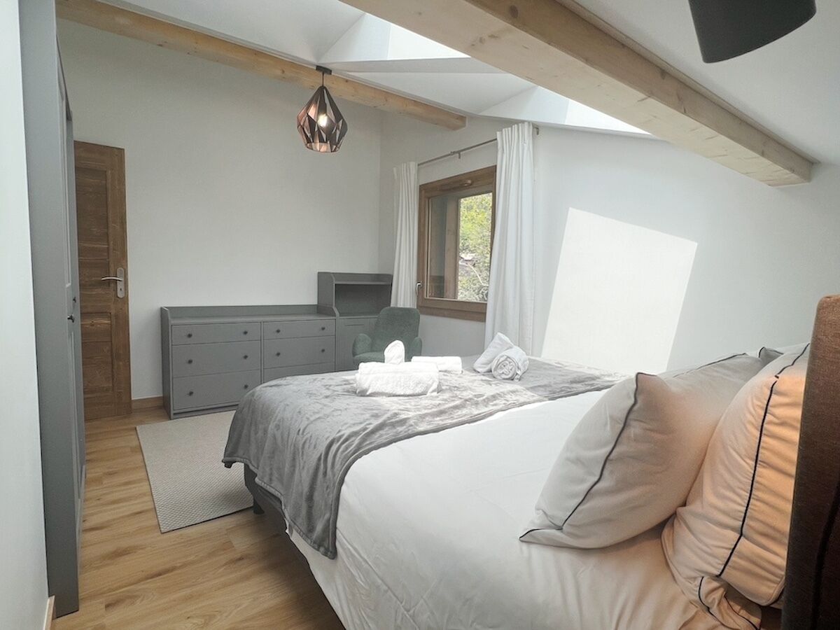 Une chambre à coucher avec un lit, une commode, une chaise et une fenêtre.