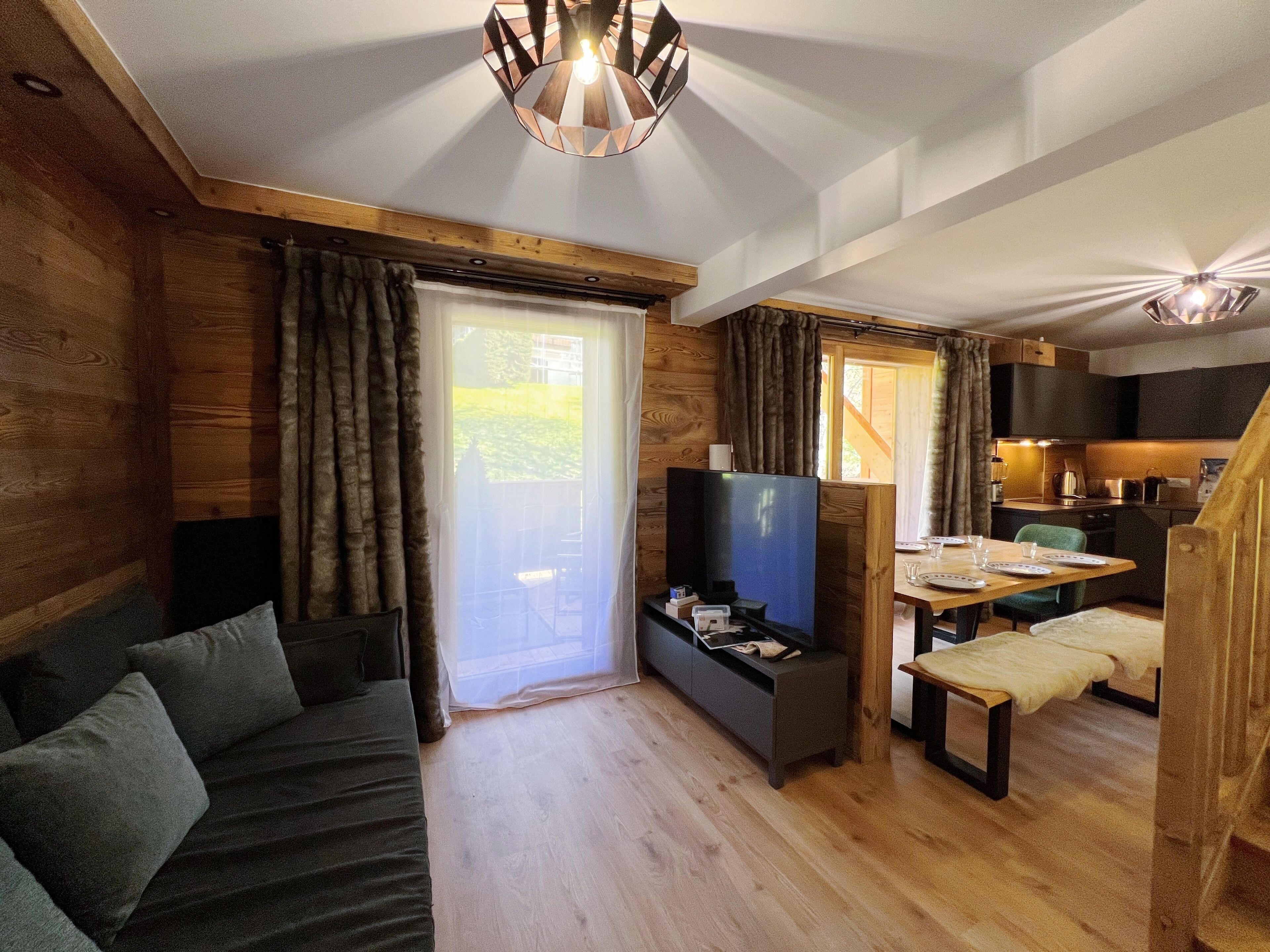 Ein gemütliches Blockhaus-Interieur mit Holzvertäfelung, einer Couch, einem Fernseher, einem Esstisch und einer Küchenzeile.