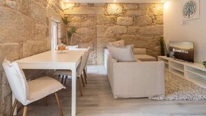A cozy living room with a stone wall, a dining table with chairs, a sofa, and a TV on a stand. - Comfy Flat | Jacuzzi & Terrace by HostWise (Porto)