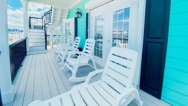 A covered porch with white plastic chairs, a staircase, and a view of the city. - Teal Tidez Ocean View Luxury Home w Crows Nest (Murrells Inlet)