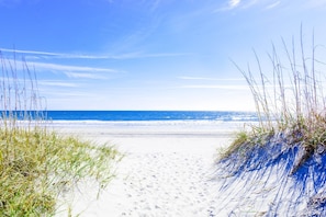 En strandpromenad som leder ner till havet, med klar himmel.