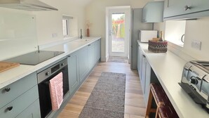 A modern kitchen with grey cabinets, a built-in oven, a stainless steel range hood, and a microwave. - Charming 3 Bed Townhouse Near Llanddwyn Beach (Llanfairpwllgwyngyll)