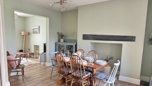 A dining area with a wooden table and chairs, a chandelier, and a fireplace. - Charming 3 Bed Townhouse Near Llanddwyn Beach (Llanfairpwllgwyngyll)