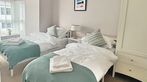 A hotel room with two beds, a nightstand with a lamp, a wardrobe, and a framed picture on the wall. - Charming 3 Bed Townhouse Near Llanddwyn Beach (Llanfairpwllgwyngyll)