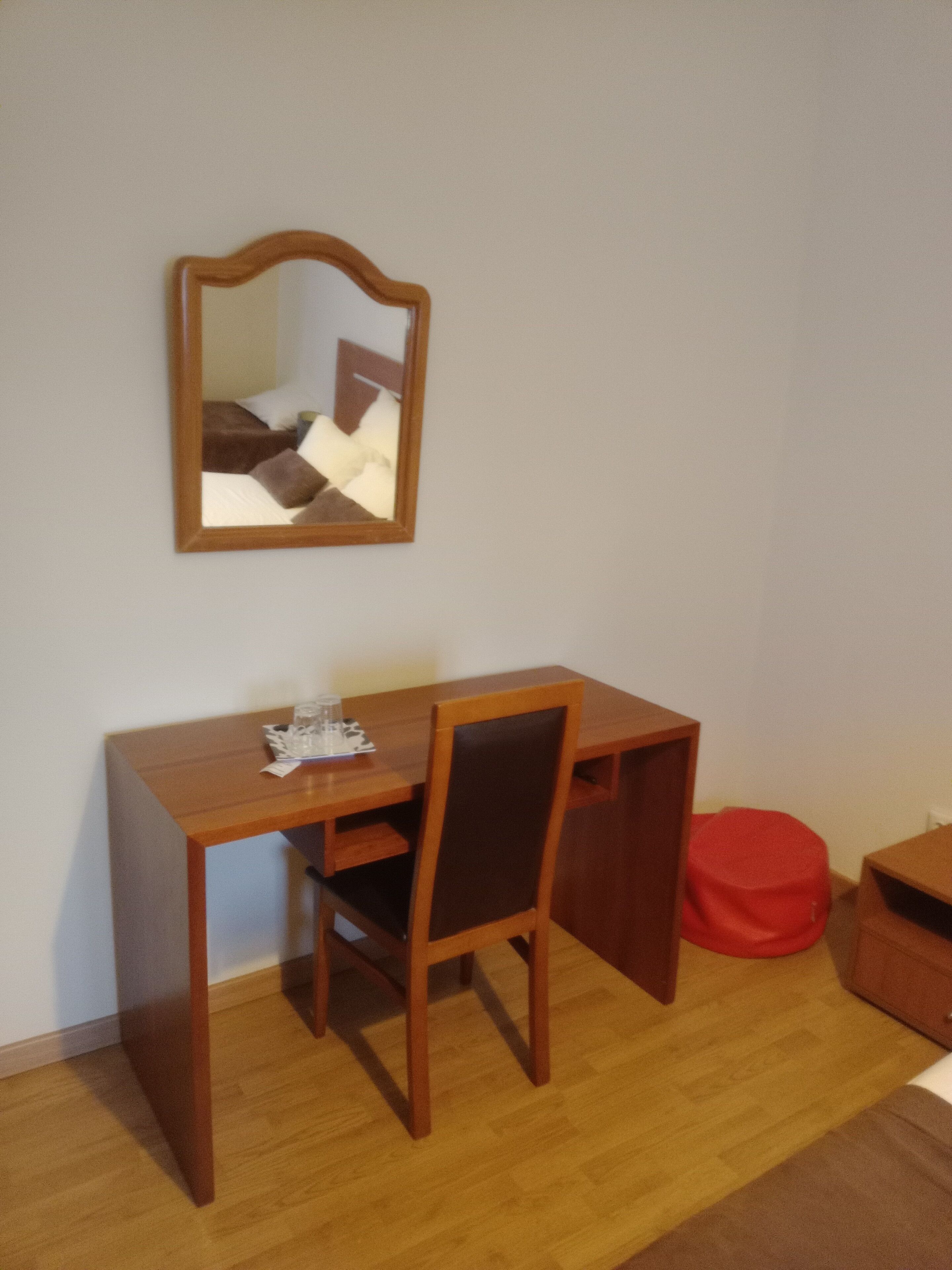 A small room with a wooden desk, a chair, a mirror, and a red bean bag.