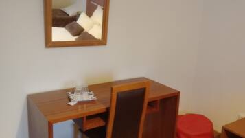 A small room with a wooden desk, a chair, a mirror, and a red bean bag.