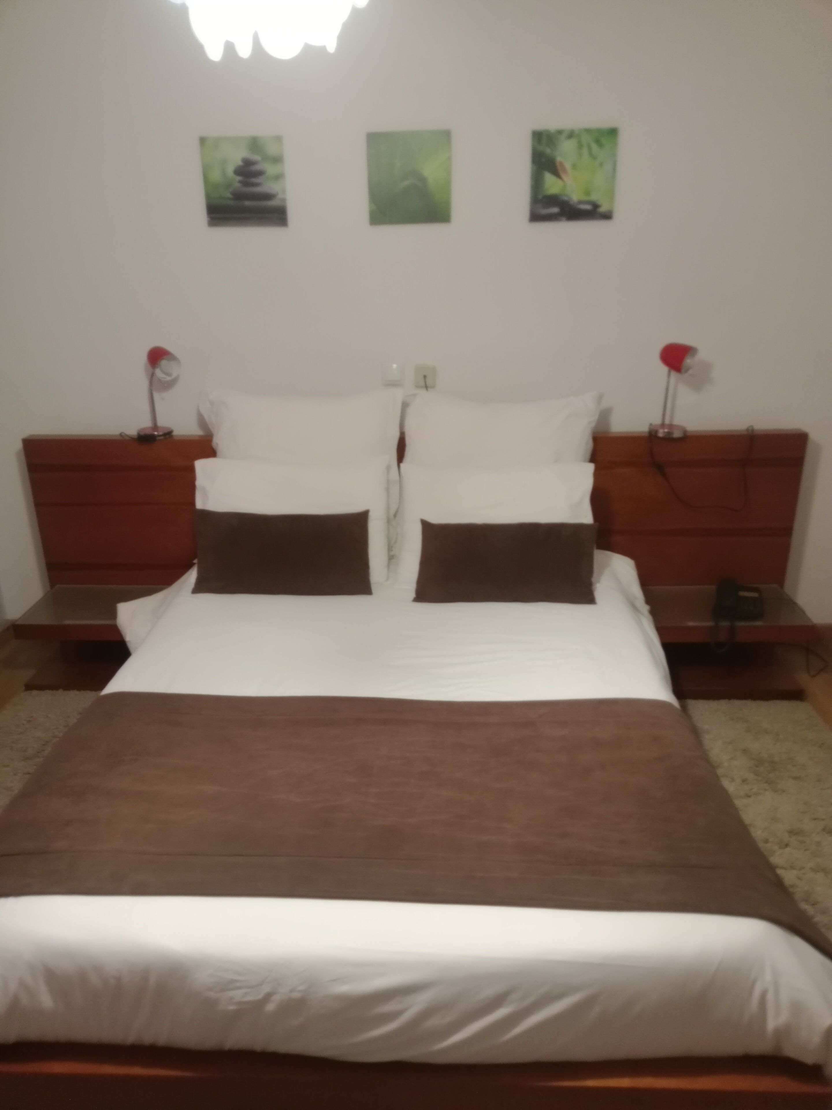 A neatly made bed with white and brown bedding, two bedside tables with lamps, and three framed pictures on the wall.