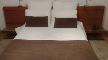 A neatly made bed with white and brown bedding, two bedside tables with lamps, and three framed pictures on the wall.