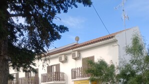 A building with balconies, a sign for 'Dormidas Rooms', and outdoor seating.