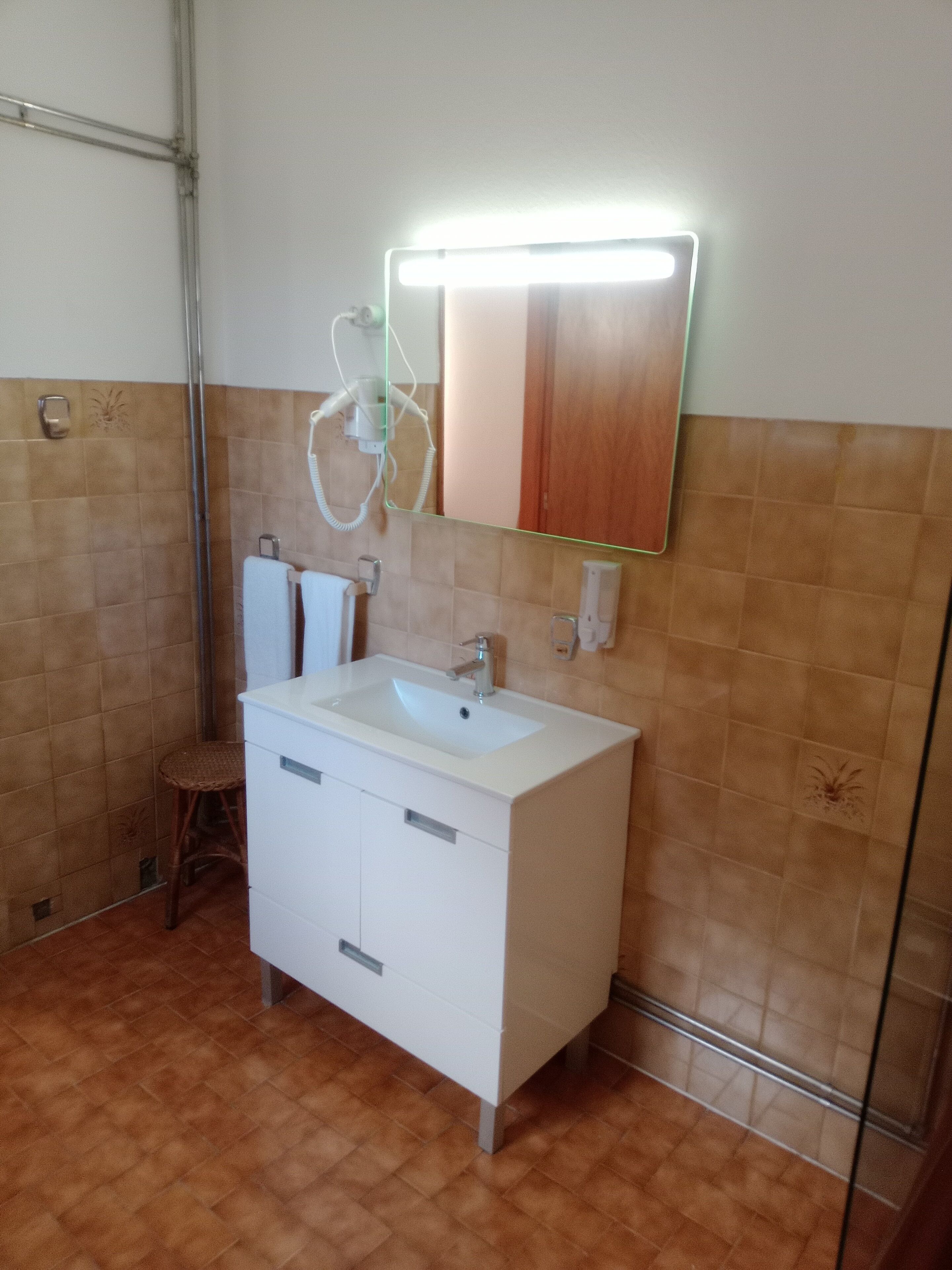 Un baño con un lavamanos blanco, un espejo y un perchero para toallas.