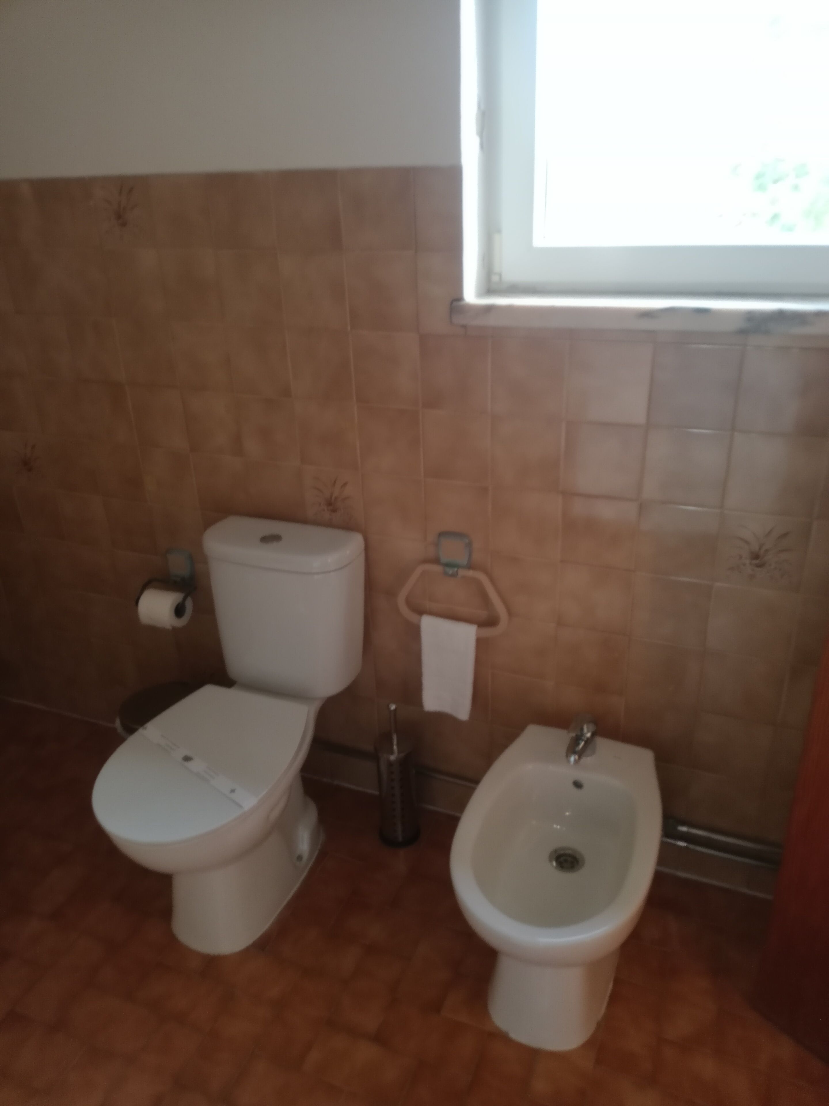 A bathroom with two toilets, a bidet, and a window.