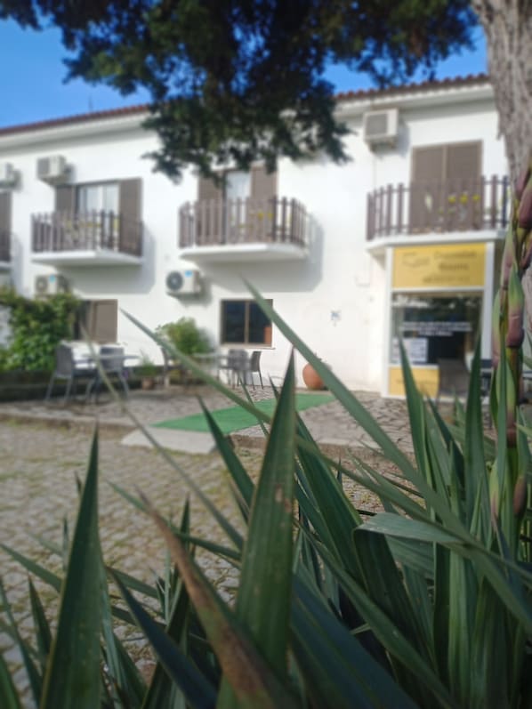 A courtyard with a building featuring balconies and outdoor seating. - Residencial Morgado (Almeida)
