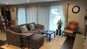 A living room with a sofa, coffee table, and a chair. There is a clock on the wall and a plant on a side table. - Beautiful deck overlooking Maple Lake with private, shared dock. (Maple Lake)