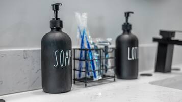 Un baño con encimera de mármol, dos dispensadores de jabón etiquetados 'SOAP' y 'LOT', y un porta cepillos de dientes con cepillos de dientes azules.