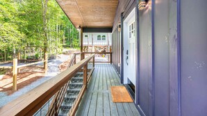 Une terrasse en bois couverte, dotée d’une rambarde en métal, qui mène à un bâtiment à la façade bleue.