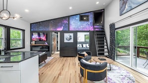 Un intérieur moderne comprenant une cuisine, un coin repas et une chambre à coucher avec un mur décoré sur le thème de la galaxie.