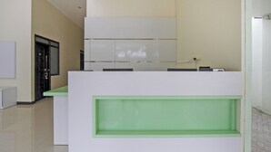 A reception desk with a green accent, a white wall, and a black-framed window. - Hotel O Irma's Residence (Blitar)