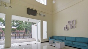 A spacious living room with a blue sofa, a coffee table, and a large window providing natural light. - Hotel O Irma's Residence (Blitar)