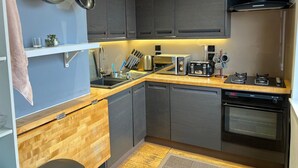 Una cocina compacta con gabinetes grises, encimera de madera, lavavajillas integrado, estufa y tostadora.