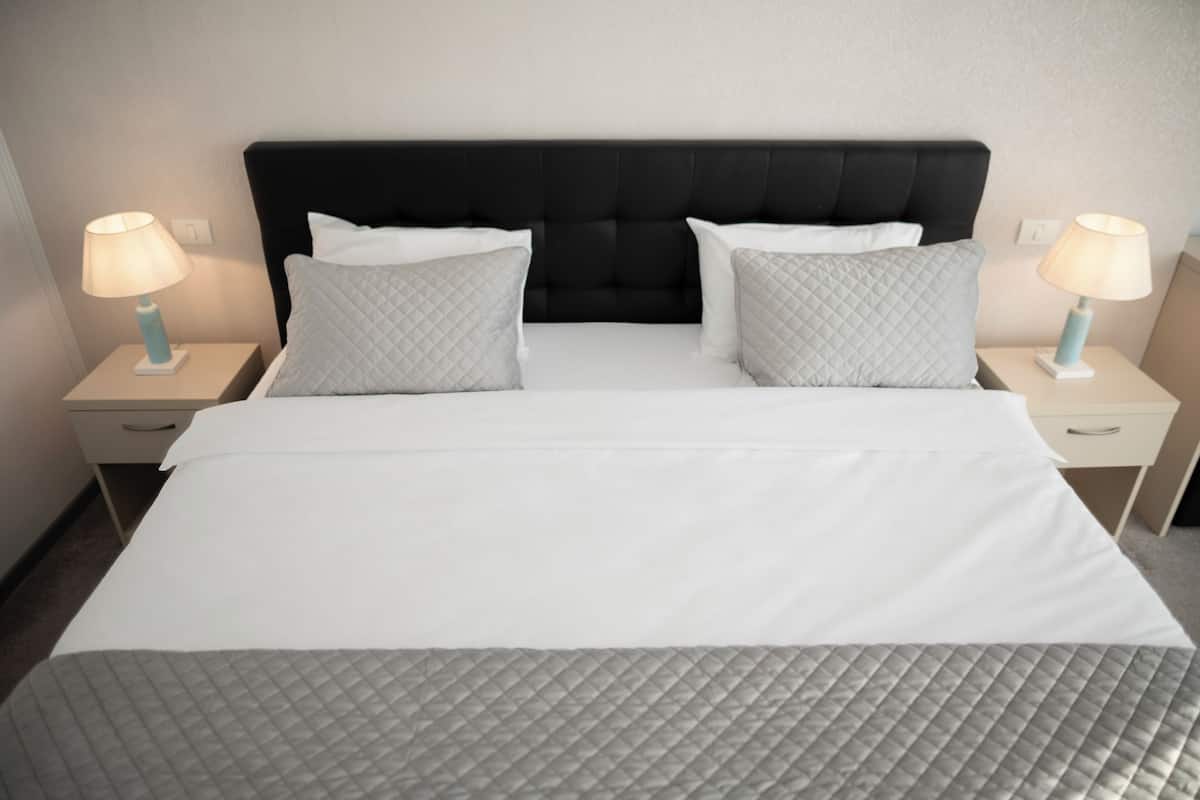 A hotel room with a black upholstered headboard, two bedside tables with lamps, and a bed with a quilted gray bedspread.