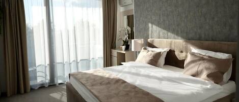 Habitación de hotel con una cama grande, una mesita de noche, una lámpara y vistas a la ciudad desde la ventana.