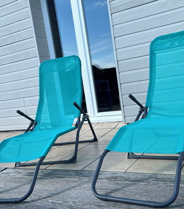 Two teal lounge chairs with black metal frames on a tiled patio.