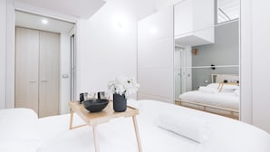 Ein modernes Schlafzimmer mit einem hölzernen Bett, einem Nachttisch mit Schale und Blumen, einem Spiegel und einem Kleiderschrank.
