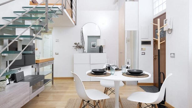 Eine moderne Küche mit Essbereich, ausgestattet mit einem runden Tisch, weißen Stühlen und einer Treppe mit Glasgeländern.