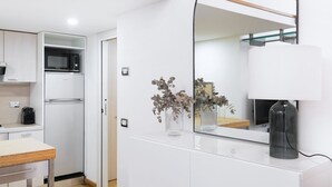 Eine moderne Küche mit weißen Schränken, einer Mikrowelle und einem Kühlschrank. Ein Esstisch mit Stühlen sowie ein Spiegel an der Wand sind ebenfalls vorhanden.