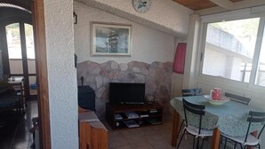 Ein gemütliches Wohnzimmer mit Kamin aus Naturstein, einem Flachbildfernseher und einem Essbereich mit Tisch und Stühlen.