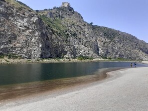 Une colline rocheuse, avec un petit bâtiment au sommet, et une étendue d’eau calme au premier plan.