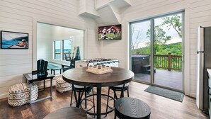 A spacious room with a round table, chairs, a foosball table, a television, and a large sliding glass door leading to an outdoor deck. - Douglas Lake Life and Pigeon Forge Adventures (Sevierville)