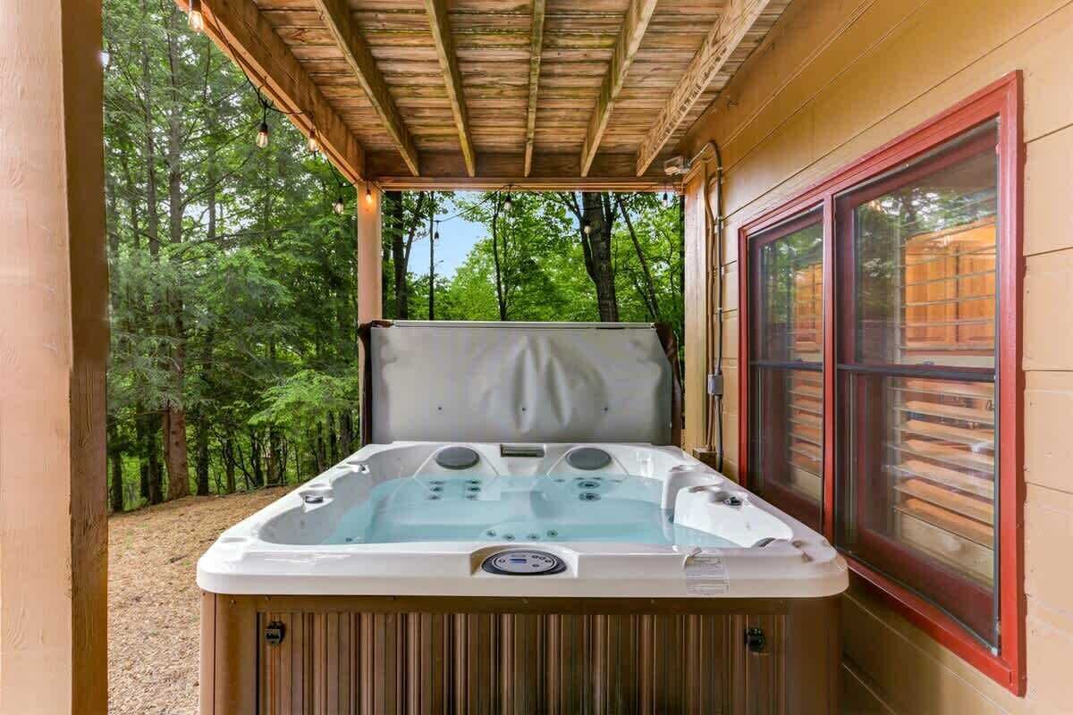 A hot tub in a covered outdoor area with a wooden ceiling and a window with blinds.
