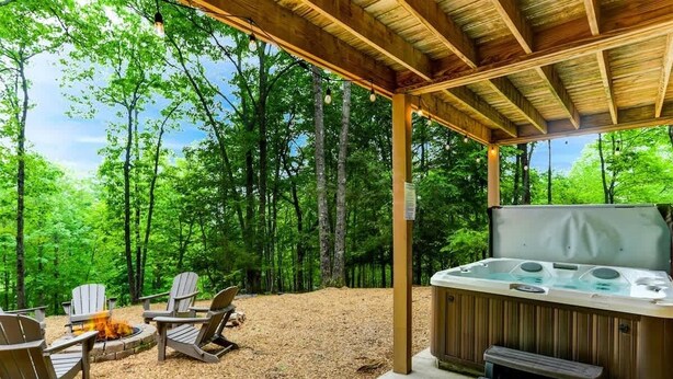 Un área de hidromasaje al aire libre con sillas Adirondack y una chimenea, rodeada de zonas boscosas.