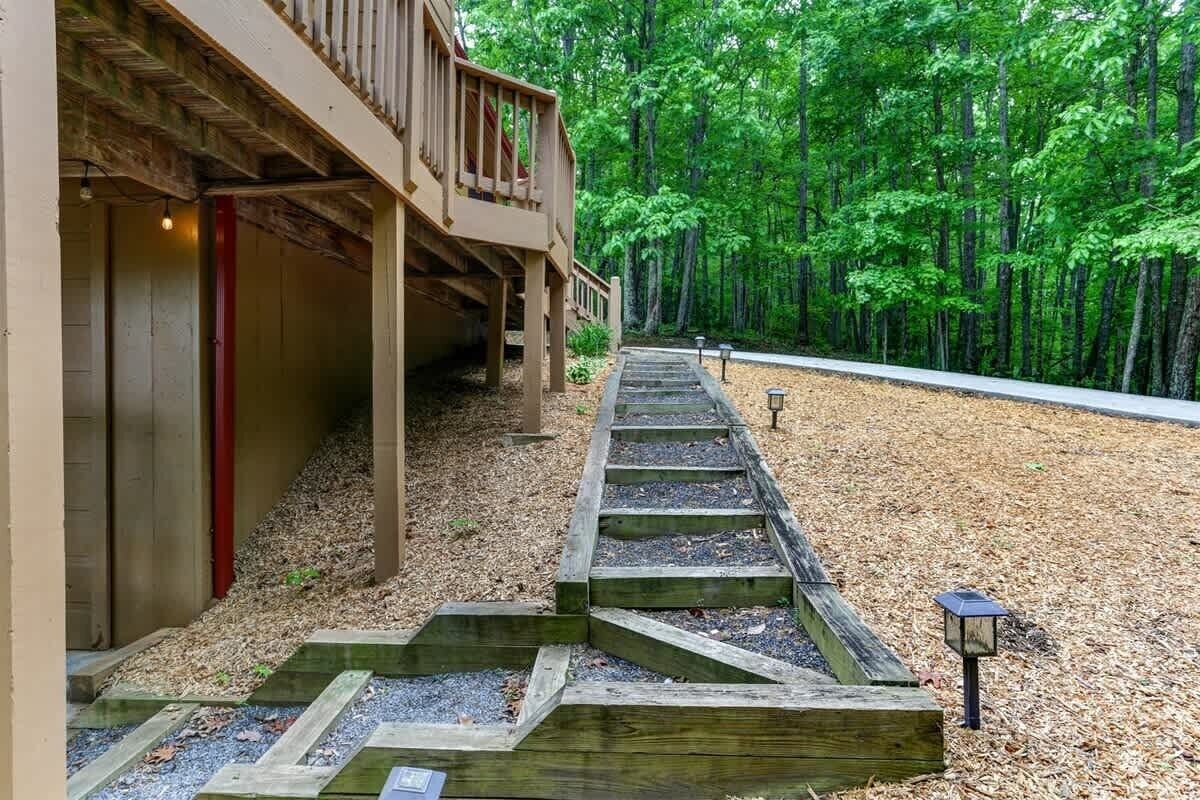 A wooden staircase leading to a building with a balcony, surrounded by a forested area.