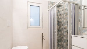 Une salle de bain avec des toilettes, une douche dotée d’une porte en verre et un mur carrelé.