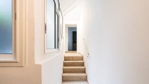Un couloir étroit et bien éclairé, avec des marches en bois menant à une porte au fond.