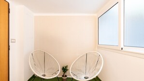 Une petite pièce avec deux chaises en osier blanches, une petite plante en pot et une fenêtre.