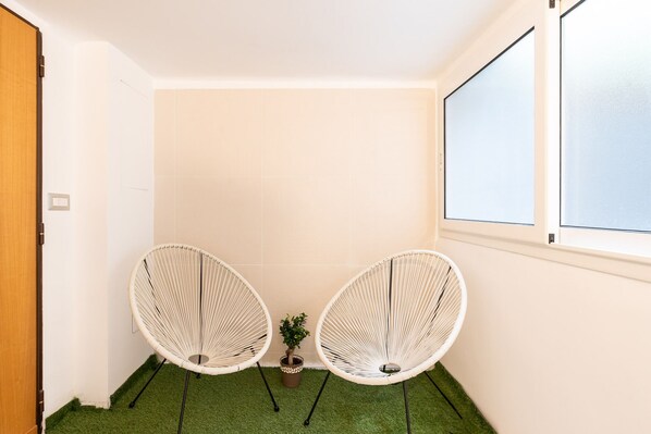 Una habitación pequeña con dos sillones blancos de mimbre, una pequeña planta en maceta y una ventana.