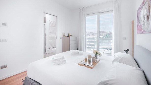 Una habitación de hotel moderna con una cama grande, vistas a la ciudad y un balcón.
