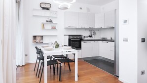 Una cocina moderna con armarios blancos, una mesa de comedor con sillas y un reloj en la pared.
