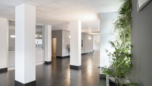Un vestíbulo amplio con pilares blancos, piso de baldosas y plantas de interior.