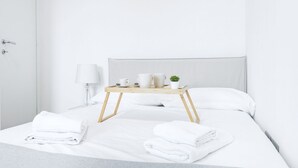 Una cama bien hecha con sábanas blancas, una mesita de noche con lámpara y una bandeja con tazas y una planta.