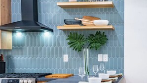 A modern kitchen with a wooden island, bar stools, a gas stove, and a blue tiled backsplash.